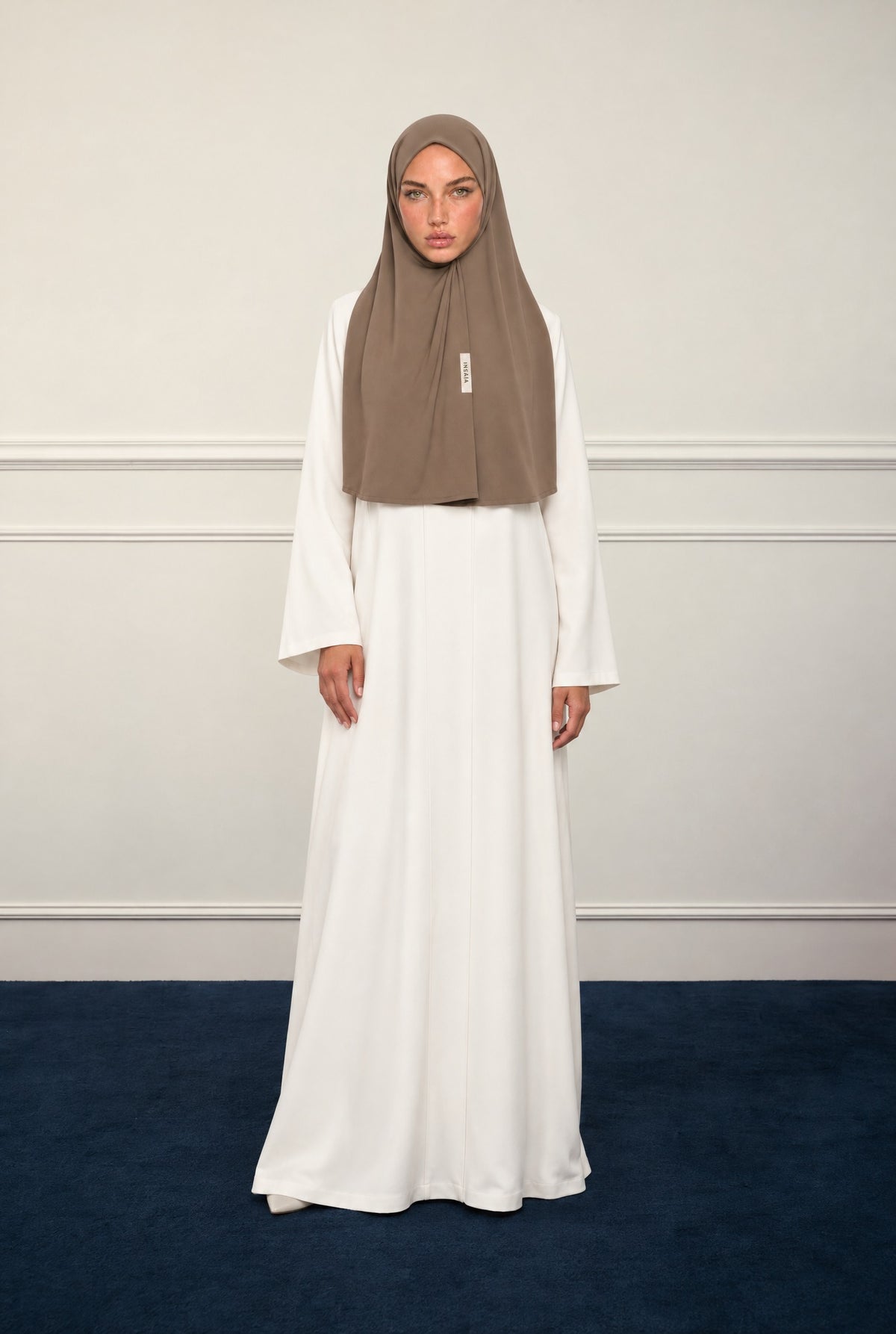 Model in the INSAÏA Taupe jersey scarf and a long white dress in a classic panelled room